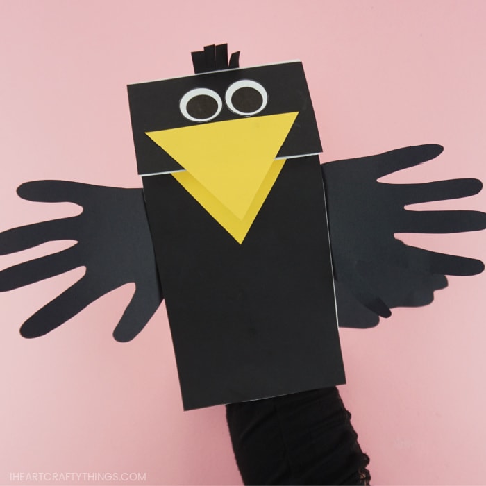 Adult with their hand inside the paper bag crow puppet showing how to make the beak open and close.